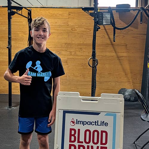 Young man standing next to blood drive sign with a thumbs up