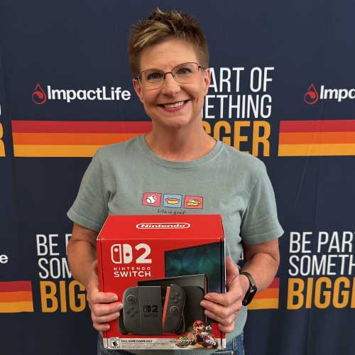 woman with glasses holding nintendo switch 2 in front of impactlife branded backdrop