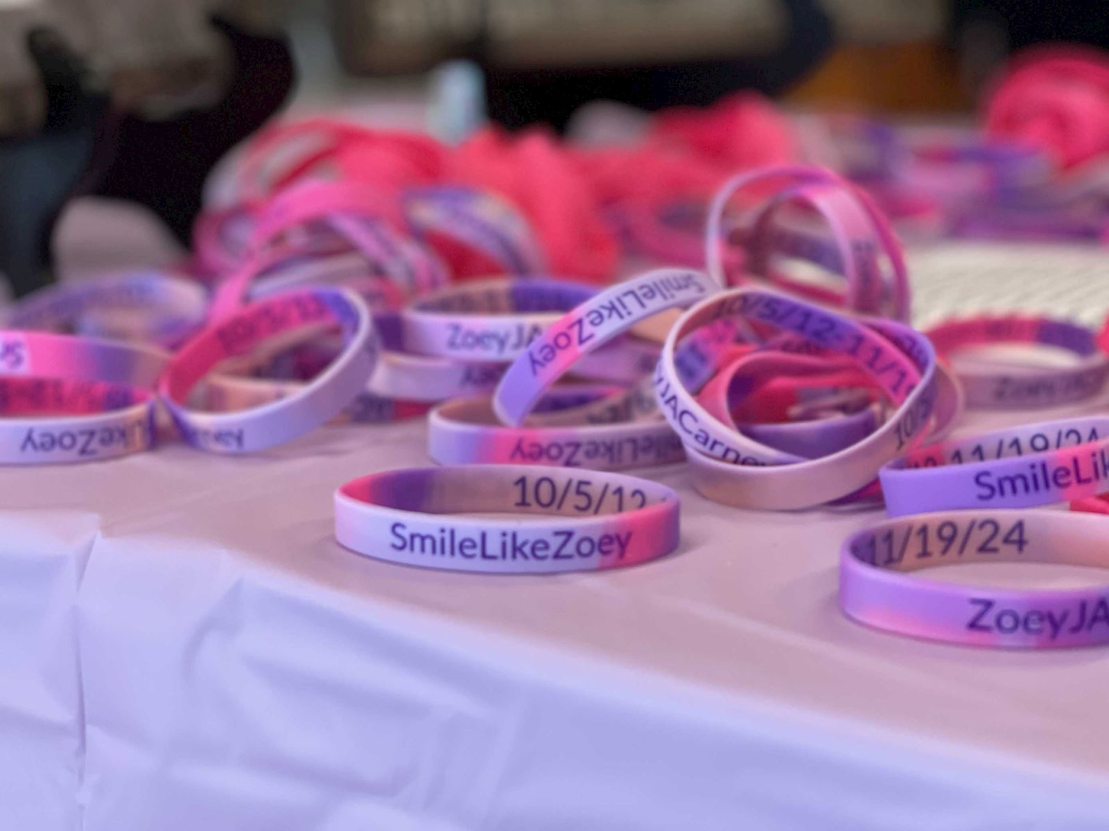 Close-up of pink and purple 'SmileLikeZoey' bracelets on a table at the ImpactLife blood drive.