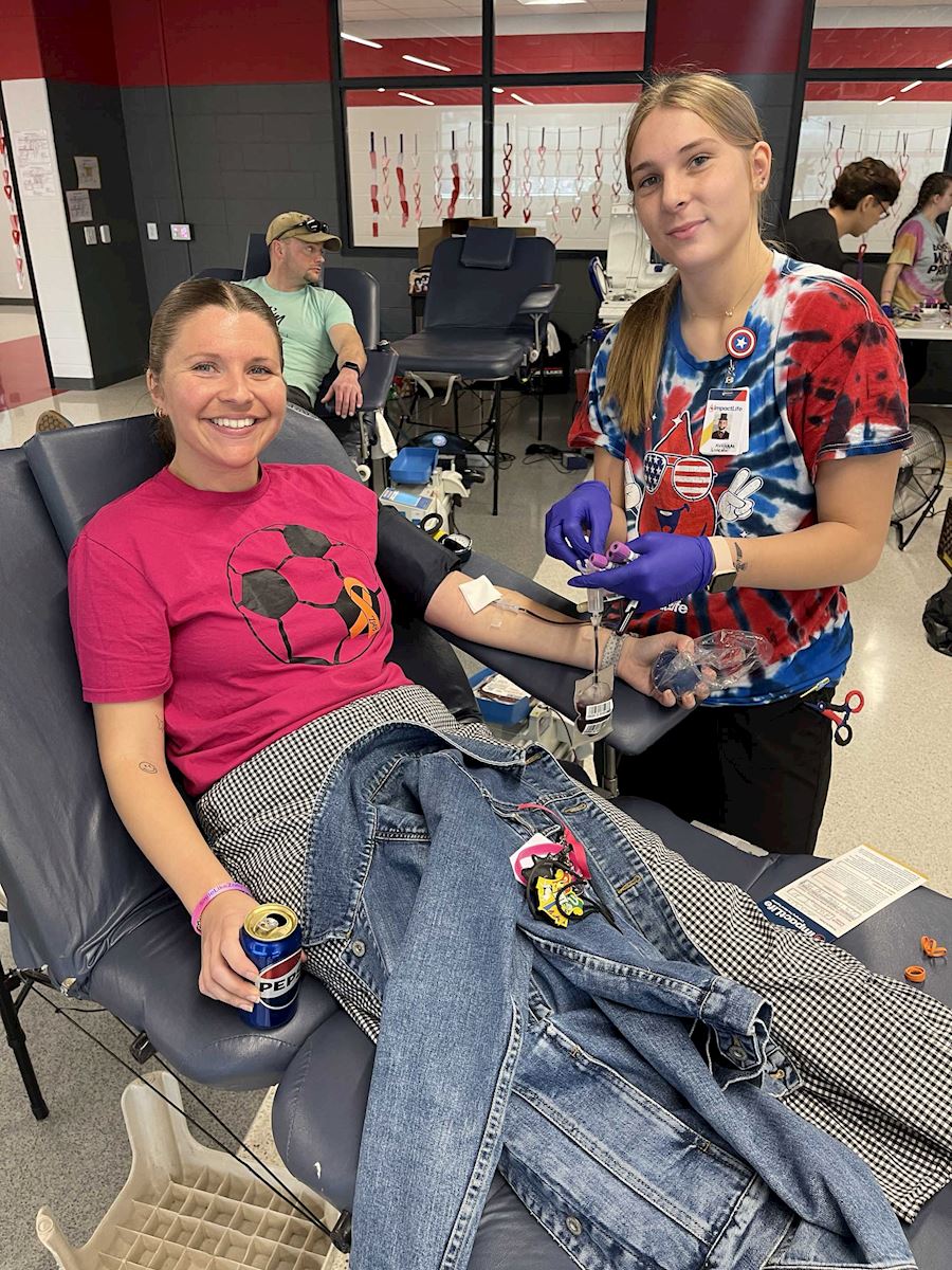 Female donor in a pink soccer shirt being assisted by staff at the ImpactLife blood drive.