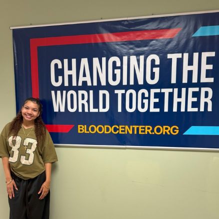 Sydnie standing in front of Changing the World Together sign at ImpactLife