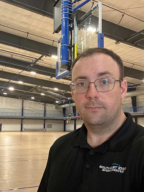 Portrait of a man wearing glasses standing on an indoor basketball court