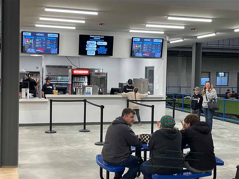 Concession stand area with menu boards and patrons seated at blue picnic tables